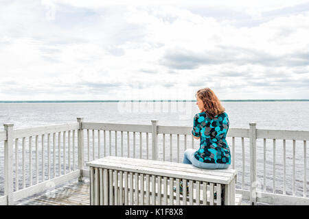 Junge Frau auf weiße Sitzbank mit Blick auf den friedlichen Saint Lawrence Fluss in Québec, Kanada sitzen Stockfoto