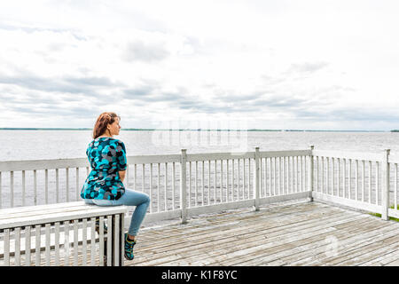 Junge Frau auf weiße Sitzbank mit Blick auf den friedlichen Saint Lawrence Fluss in Québec, Kanada sitzen Stockfoto