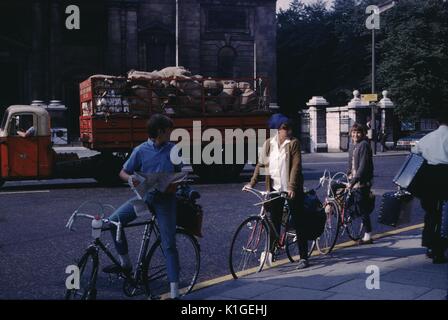 Drei junge Rucksacktouristen auf Fahrräder, an der Seite von einer Straße in einem Stadtzentrum Lesen einer Karte geparkt, einen roten cargo Lkw im Hintergrund, Schottland, 1966. Stockfoto