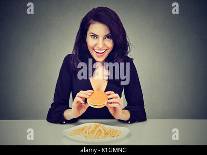 Sie mag fast food. Glückliche Frau essen Cheeseburger und Pommes frites Stockfoto