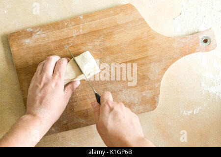Ansicht von oben Schießen von Menschenhänden Schneiden von rohem Teig auf dem Tisch Stockfoto