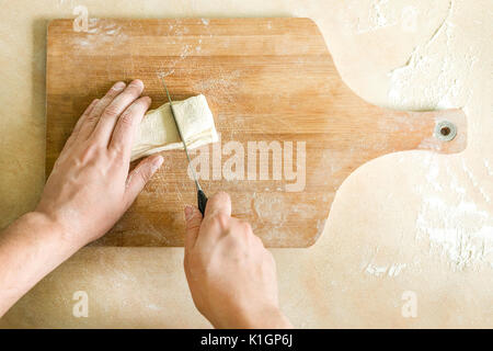 Ansicht von oben Schießen von Menschenhänden Schneiden von rohem Teig auf dem Tisch Stockfoto