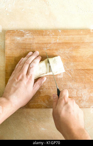 Ansicht von oben Schießen von Menschenhänden Schneiden von rohem Teig auf dem Tisch Stockfoto