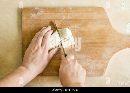 Ansicht von oben Schießen von Menschenhänden Schneiden von rohem Teig auf dem Tisch Stockfoto