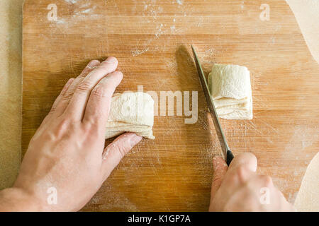Ansicht von oben Schießen von Menschenhänden Schneiden von rohem Teig auf dem Tisch Stockfoto