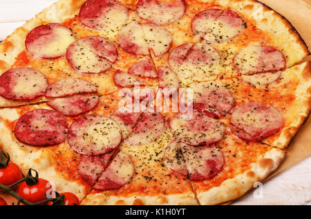 Pizza mit Tomate, Salami auf einem Tisch Stockfoto