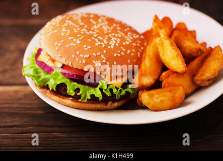 Big leckere Burger mit Rindfleisch, Tomaten, Käse, Zwiebeln und Salat mit Pommes frites in der Platte auf dem hölzernen Tisch Stockfoto