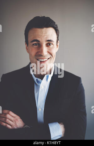 Porträt einer selbstbewussten jungen Geschäftsmann trägt einen Blazer, die alleine stehen in einem Büro mit verschränkten Armen Stockfoto