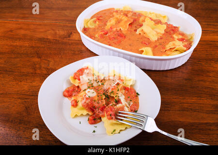 Hausgemachte Ravioli mit Tomaten-sahne-Soße in eine weiße Platte und Auflauf mit Gabel auf Holz Tisch Stockfoto