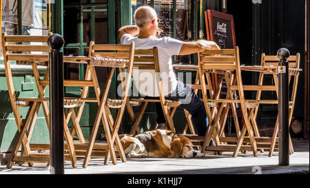 Cafe/Bar Eigentümer draußen sitzen in der warmen September Sonnenschein unter den Tisch und Stühle, mit seinem Hund schläft auf dem Bürgersteig. Paris, Frankreich, Europa. Stockfoto