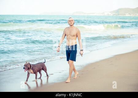 Junger Mann mit Hund American Pit Bull Terrier zu Fuß am Meer Stockfoto