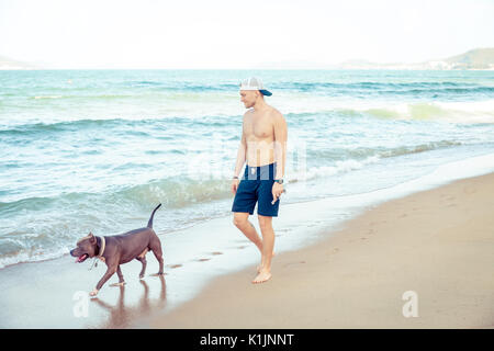 Junger Mann mit Hund American Pit Bull Terrier zu Fuß auf den tropischen Strand Stockfoto