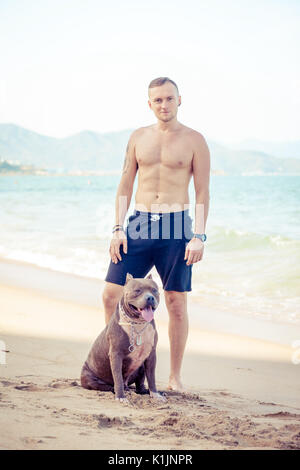 Junger Mann mit Hund American Pit Bull Terrier am tropischen Strand posiert Stockfoto