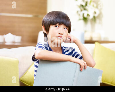 Kleine asiatische Kind sitzen auf der Couch, die ein Buch suchen und Denken. Stockfoto