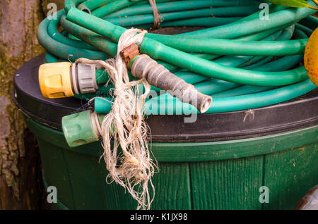 Einen alten Schlauch mit Tippen Sie auf Anschlüsse und eine Sprühdüse eingerollt und links oben auf ein Fach in einem Garten auf der Rückseite. Stockfoto