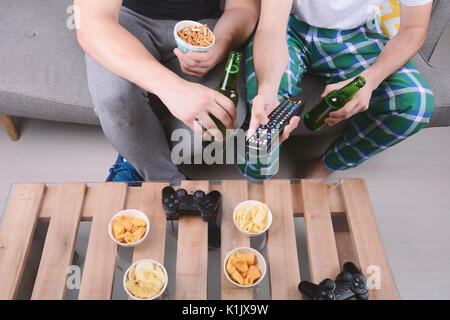 Porträt von zwei Freunden, die Videospiele, essen Snacks und drinkng Bier. Im Innenbereich. Stockfoto