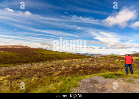 Malerische Aussicht auf die schöne Natur des Cairgorms National Park in Schottland im Sommer mit einem Mann mit einer roten Jacke im Vordergrund. Stockfoto