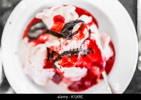 Weiche Vanille Eis mit roten Erdbeer Sauce servieren und beträufelt Schokolade Sirup Nahaufnahme in der Schüssel Stockfoto