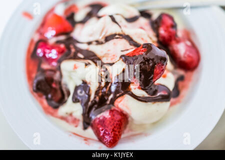 Weiche Vanille Eis mit roten Erdbeer Sauce servieren und beträufelt Schokolade Sirup closeup in Schüssel flache Ansicht von oben Stockfoto