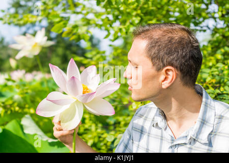 Portrait Nahaufnahme des jungen Mannes in hellem Weiß und Pink Lotus Blume mit gelben seedpod Innen suchen Stockfoto