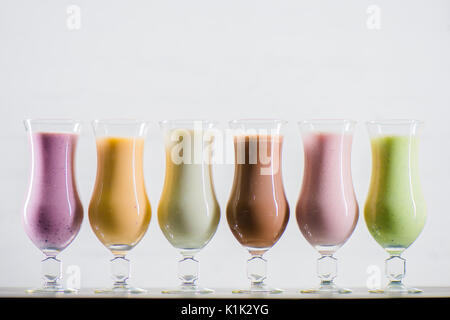 Nahaufnahme der verschiedenen leckeren Milchshakes in Gläser isoliert auf Grau Stockfoto