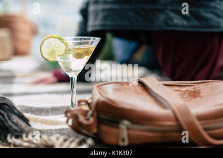 Nahaufnahme der Martini Glas mit Zitronen und Oliven auf kariertem Schottenstoff in der Nähe von Leder handtasche Stockfoto