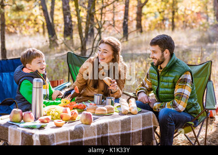 Glücklich lächelnde Familie essen und Spaß beim am Tisch sitzen auf Picknick im Herbst Wald Stockfoto