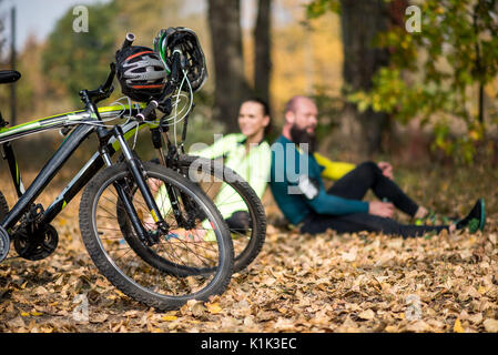 Nahaufnahme der zwei Mountainbikes mit Helmen und paar Radfahrer im Herbst Park Stockfoto