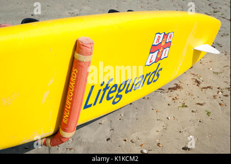 Eine gelbe RNLI Rettungsschwimmer paddle Board auf einem sandigen Strand bei Ebbe an einem Sommertag in Littlehampton, West Sussex, England. Stockfoto