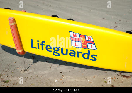 Eine gelbe RNLI Rettungsschwimmer paddle Board auf einem sandigen Strand bei Ebbe an einem Sommertag in Littlehampton, West Sussex, England. Stockfoto