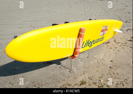 Eine gelbe RNLI Rettungsschwimmer paddle Board auf einem sandigen Strand bei Ebbe an einem Sommertag in Littlehampton, West Sussex, England. Stockfoto