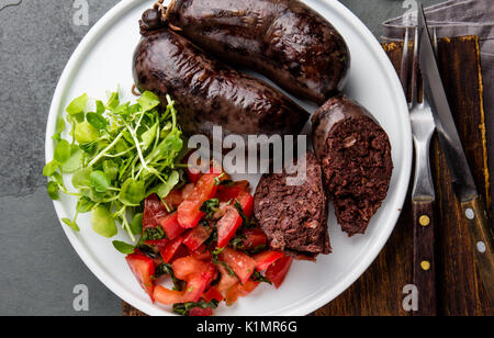 Blutige Würstchen serviert auf weiße Platte mit Salat, Ansicht von oben Stockfoto