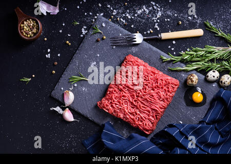 Frisches rohes Fleisch mit Gewürzen. Hackfleisch Steak auf einem dunklen Tisch. Ansicht von oben. Stockfoto