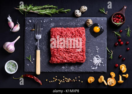 Rohe frische Lammfleisch mit Gewürzen, Zutaten zum Kochen auf schwarzem Hintergrund. Ansicht von oben, flach. Stockfoto