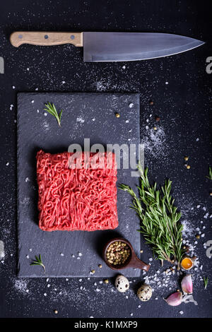 Red rohes Rindfleisch, mit Zutaten zum Kochen, serviert auf einem Stein, Küchenmesser. Ansicht von oben, kopieren. Stockfoto