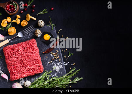 Raw saftige Hackfleisch, bratfertig auf einem schwarzen Kreidetafel Hintergrund. Rinderfilet mit Champignons Kräuter, Pfeffer und Cranberry. Platz für Text. Oben Stockfoto