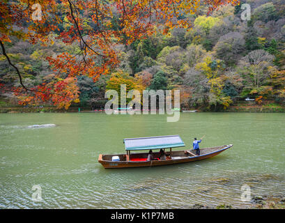 Kyoto, Japan - 28.November 2016. Boatman stochern das Boot für Touristen im Herbst Ansicht mit Ahorn Bäume entlang der Ufer des Flusses in Arashiyam Hozu zu genießen Stockfoto