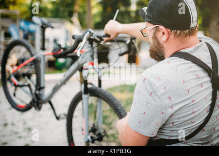 Professionellen Fahrradmechaniker in Schürze passt Bike. Zyklus Workshop Outdoor. Radfahren Sport, bärtigen service Mensch arbeiten mit Rad Stockfoto