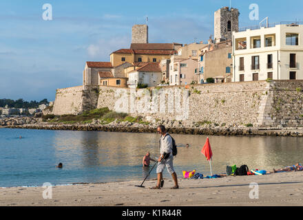 Ein Mann mit einem Metalldetektor am Strand mit Blick auf Antibes, Cote d'Azur, Frankreich Stockfoto