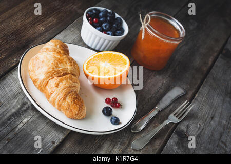 Frische Croissants, Blaubeeren, Orangen und Aprikosen Konfitüre auf rustikalen Holztisch. Winkel betrachten. Kontinentales Frühstück Stockfoto