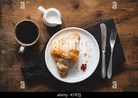 Almond Croissants, Besteck, Tasse schwarzen Kaffee Espresso und Sahne auf Holz Schneidebrett. Tabelle Ansicht von oben Stockfoto