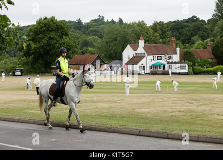 Ein Reiter passiert ein Cricket-Spiel zwischen Tilford und Greyswood, das am Samstag, den 15. Juli 2017, auf dem Grün vor dem Gerstenmähen in Tilford, Surrey, ausgetragen wird Stockfoto