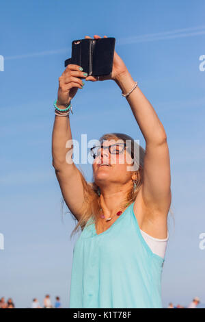 Eine junge Frau nimmt Fotos Videos mit dem Handy am Strand. Stockfoto