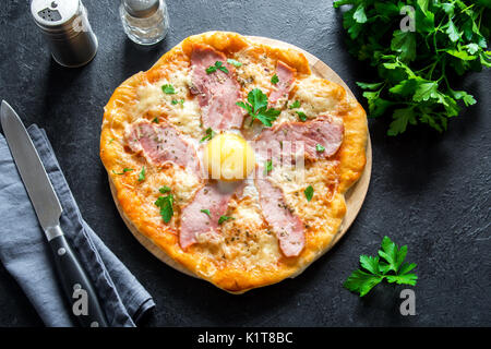 Pizza Carbonara auf schwarzem Stein. Italienische Pizza Carbonara mit Schinken, Ei und Käse. Stockfoto