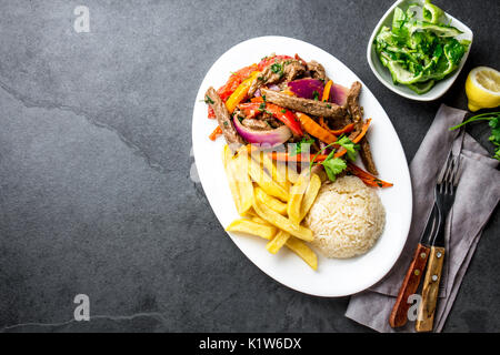 Peruanisches Gericht Lomo Saltado - Rinderfilet mit lila Zwiebel, gelbe Chili, Tomaten auf weißen Teller mit Pommes Frites und Reis serviert. Ansicht von oben Stockfoto