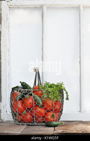 Zutaten für selbstgemachte Salsa in einem alten Korb sitzen vor einem Fenster. Stockfoto