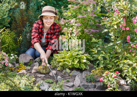 Junge Frau Gärtner Pflege von Blumen im Garten. Mädchen jäten Unkraut im Beet. Menschen, Gartenbau, Pflege von Blumen, Hobby- Konzept Stockfoto