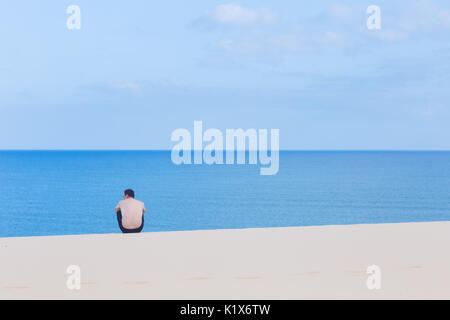 Eine minimalistische Komposition von ein Mann sitzt auf einer Düne auf dem Weg zu einer blauen Meer in Jericoacoara, Ceará, Brasilien Stockfoto
