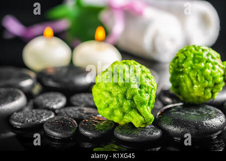 Spa Zusammensetzung der Bergamotte Früchte, Blätter, Kerzen, weiße Handtücher und zen Basaltsteine mit Wassertropfen auf schwarzem Hintergrund Stockfoto