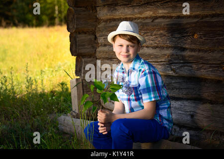 Adorable Junge in Hut duftende Flieder einen Strauß Blumen in der Landschaft. Stockfoto